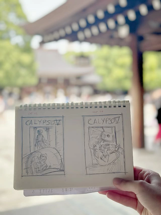 Hand holding sketches of cover illustrations against the background of Meiji Jingu in Tokyo